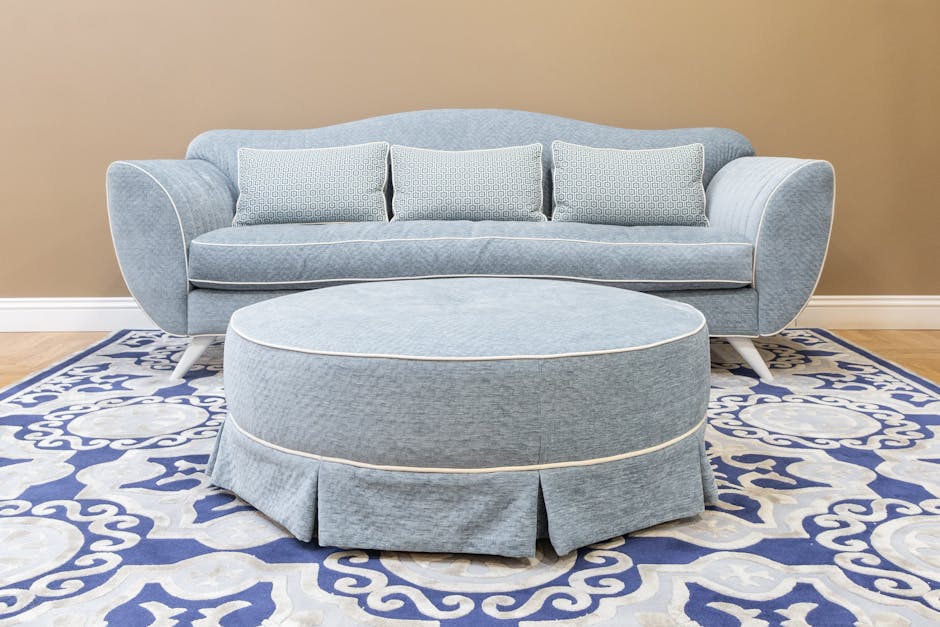 A stylish blue sofa with matching ottoman and decorative rug in a modern living room setting.